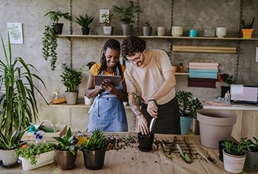 Diverse plant shop business owners looking at tablet and potting plants