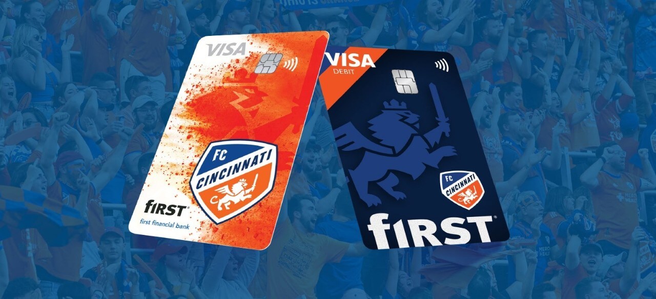 First Financial Bank FC Cincinnati credit and debit cards over orange and blue diagonal lines on a dark blue background