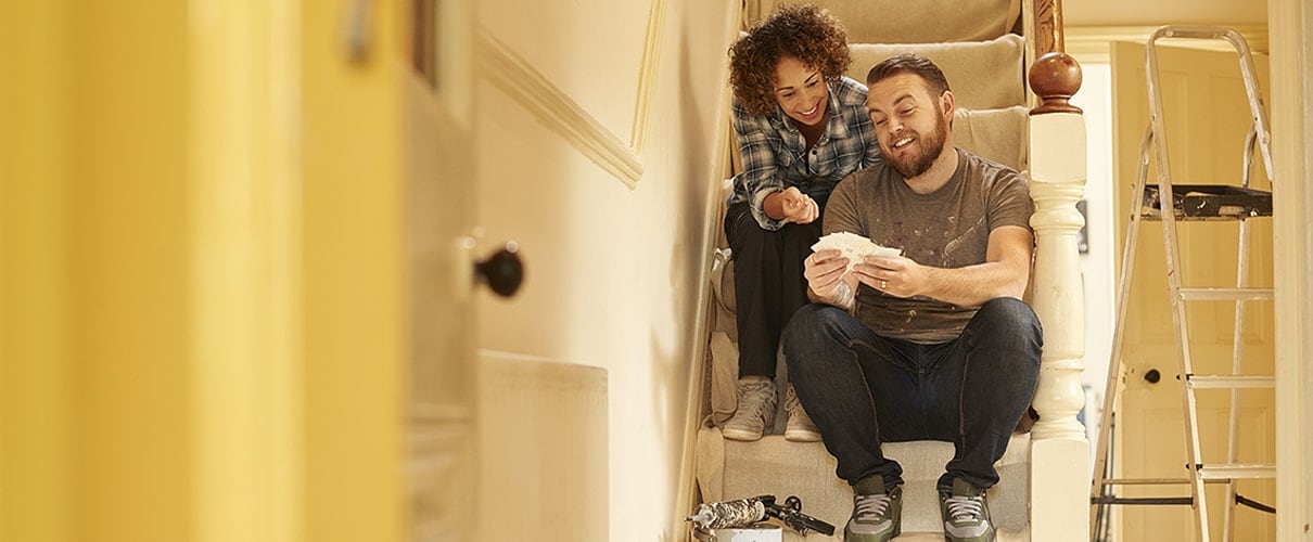 Mixed race couple renovating home sitting on steps looking at paint swatches