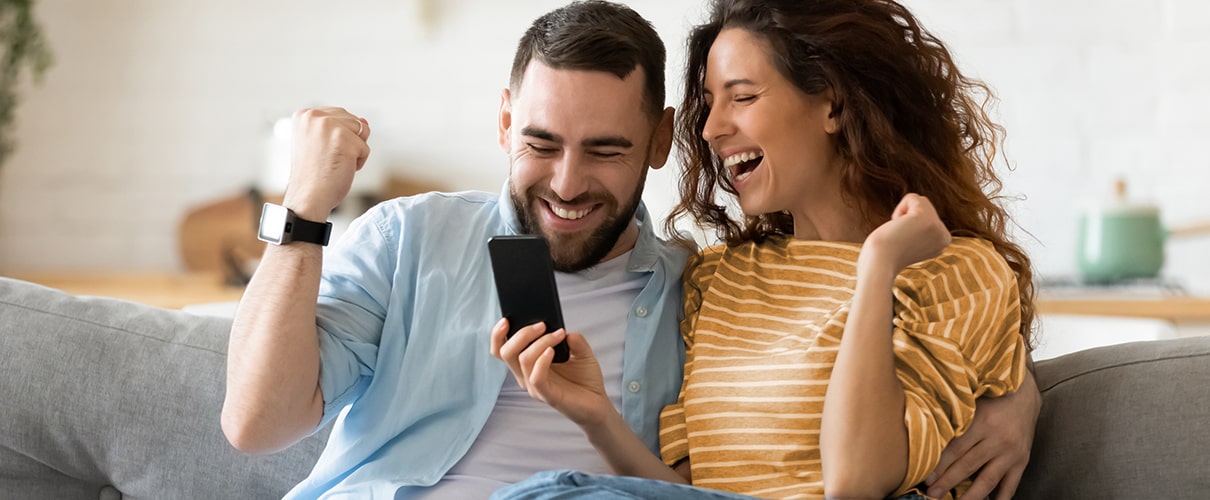 Excited couple celebrating while looking at smartphone on couch