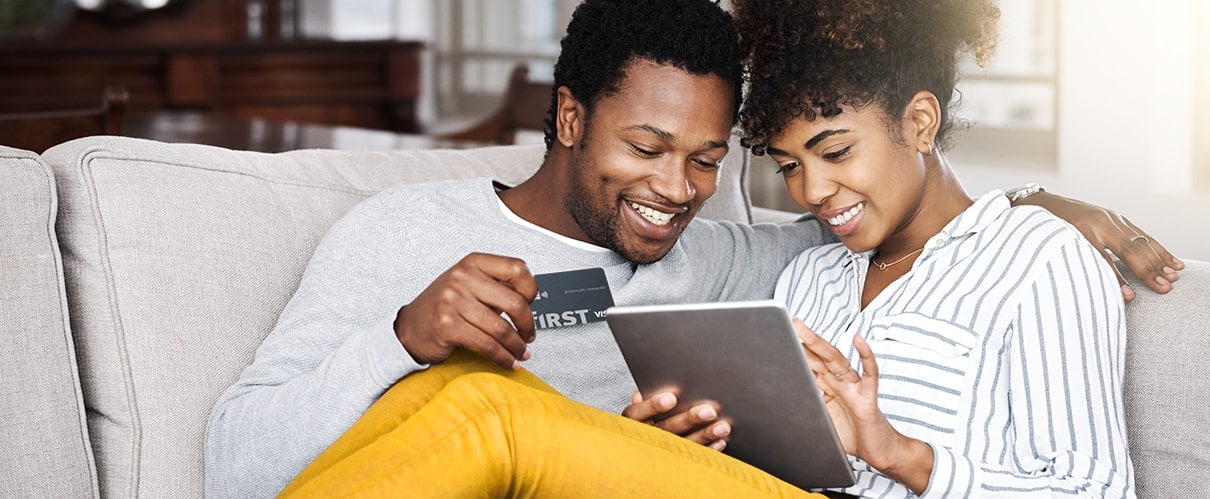 African American couple sitting on couch with man holding f1RST® Platinum card and  woman holding tablet