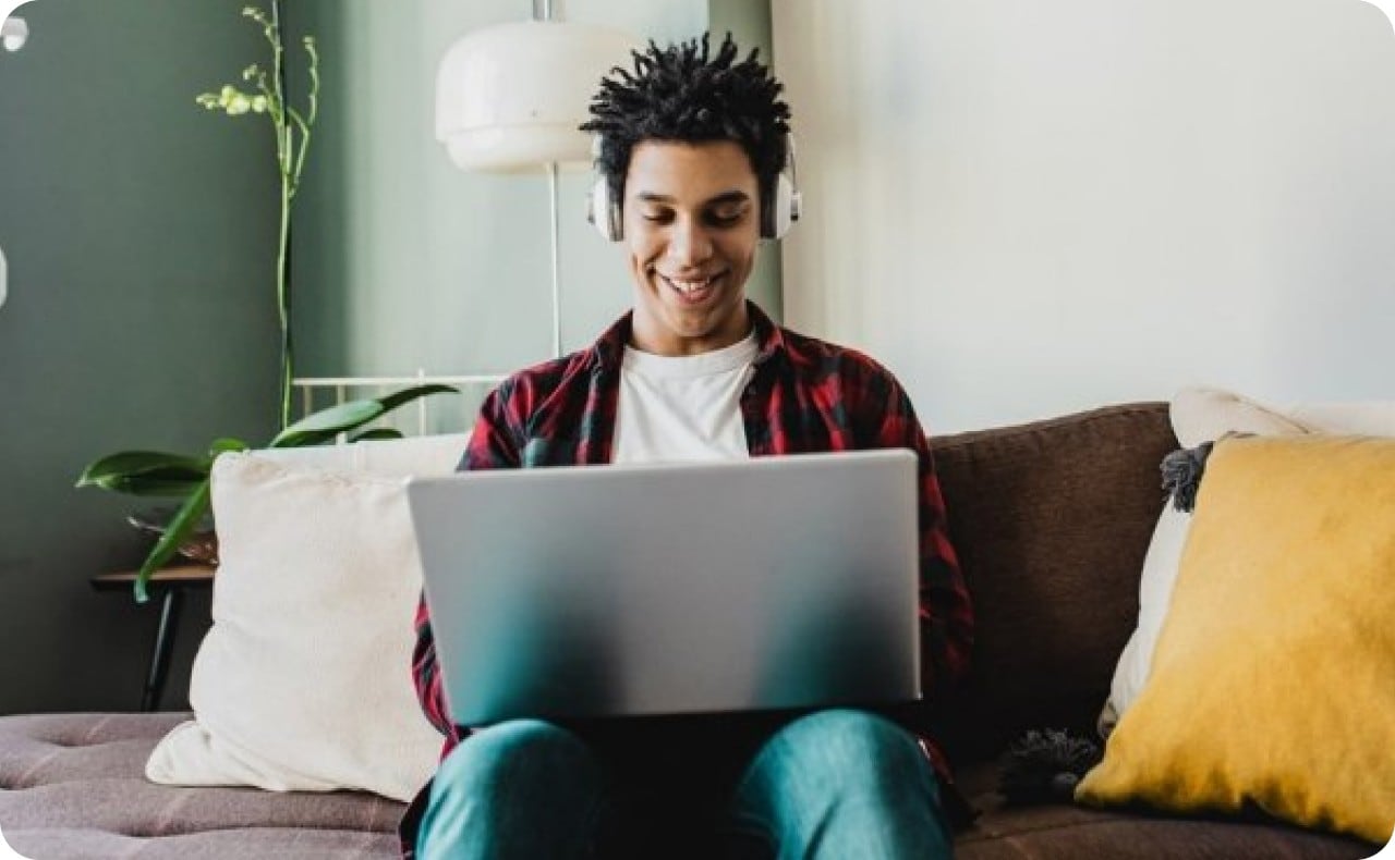 Young African-American man smiling, wearing headphones and working on laptop