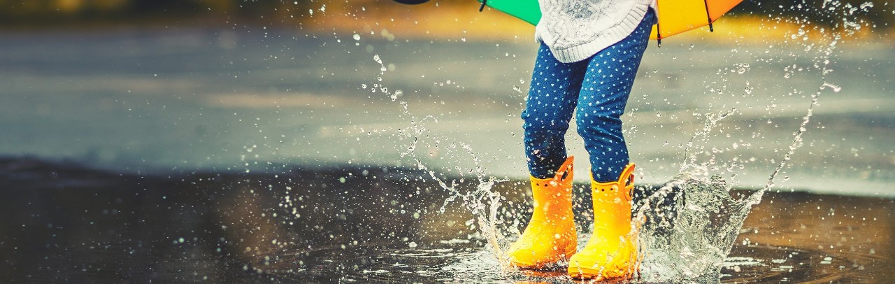 Child with yellow rainboots jumps in puddle
