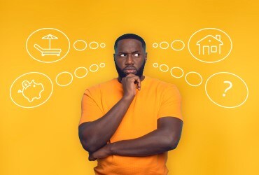 African-American man with confused look standing in front of thought bubbles including lounge chair, piggy bank, house and question mark