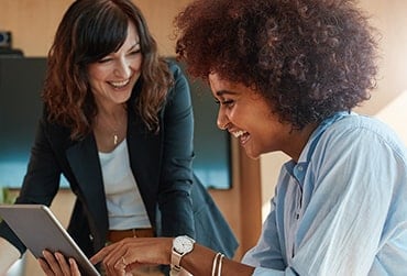 Two women smile while looking at a tablet