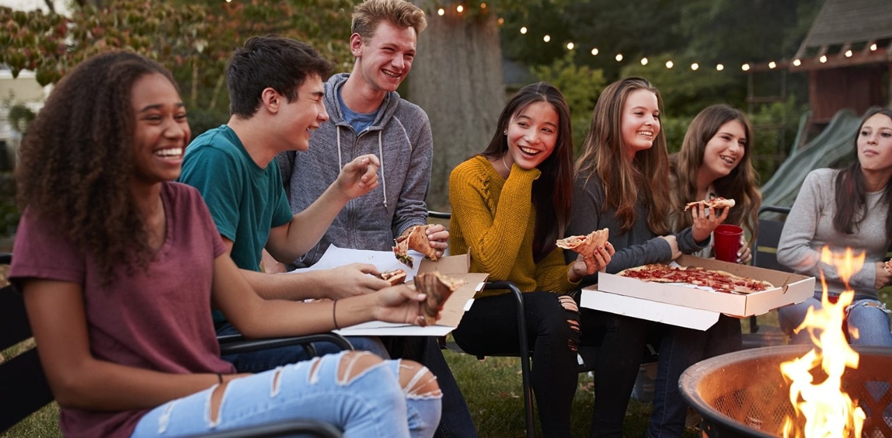 Diverse group of friends eating take-out pizza in backyard