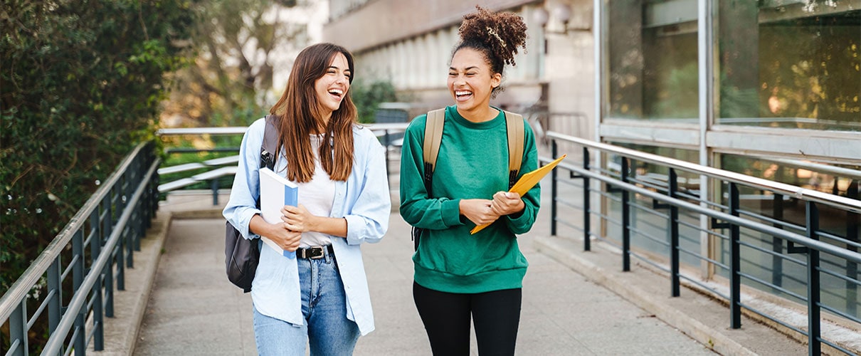 Two female students walking and smiling while carrying backpacks and books