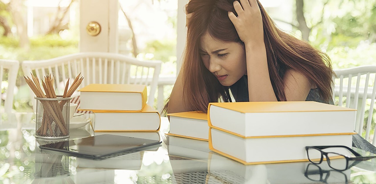 Asian woman with head in hands looking at stack of books