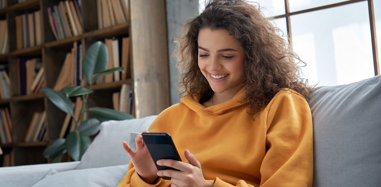 Young smiling woman using smartphone on sofa
