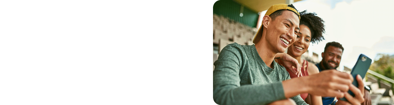 Three diverse friends sitting on stadium bleachers looking at a smartphone