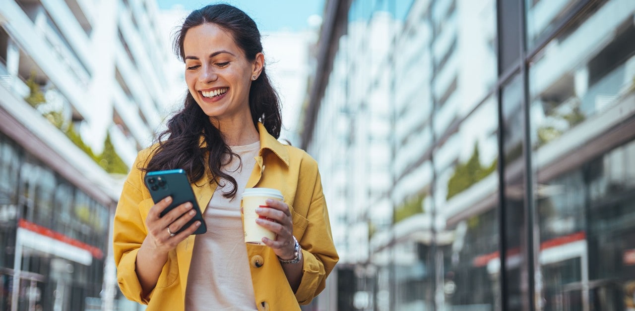 Caucasian woman smiling while holding smartphone and coffee