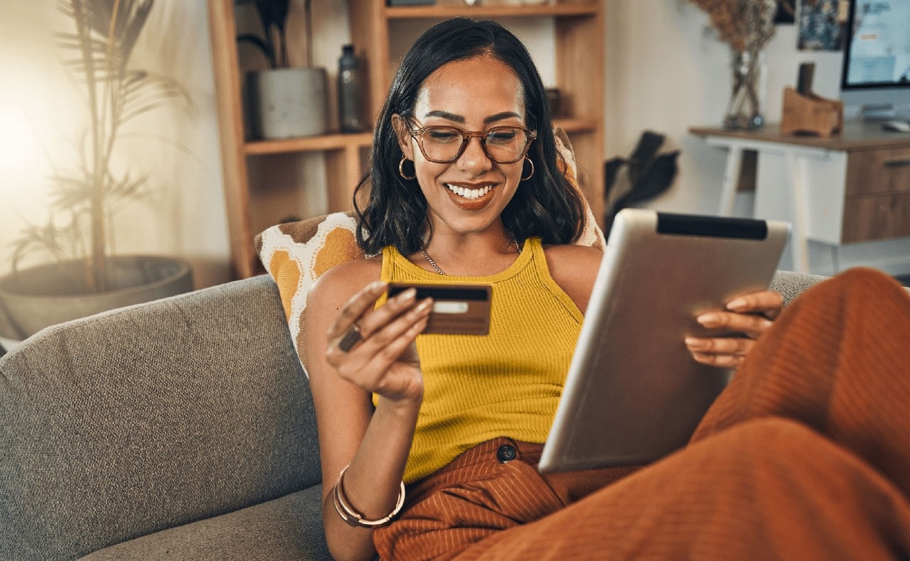 Young woman sitting on sofa holding tablet computer and debit card