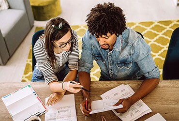 Diverse couple sitting at table reviewing financial documents