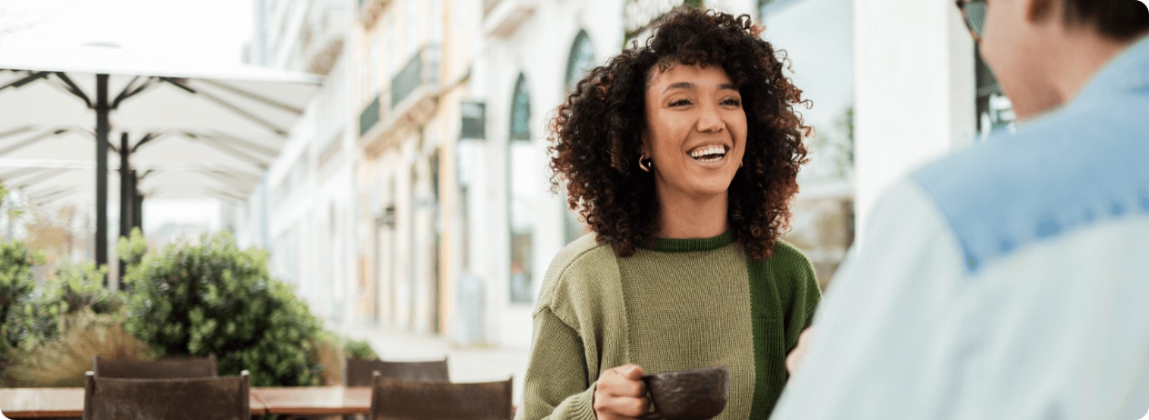 Woman holding cup of coffee looking at someone smiling with a terrace background