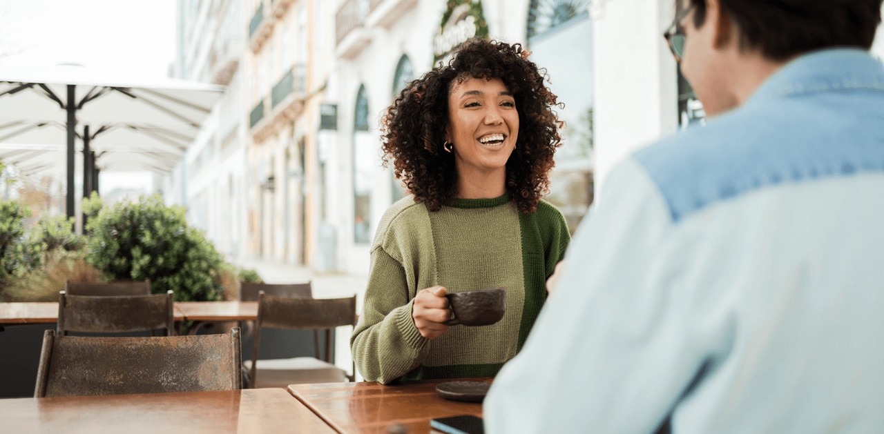 Woman holding cup of coffee looking at someone smiling with a terrace background