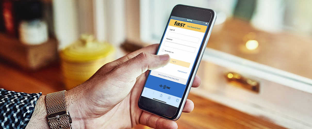 The First Financial Bank app shown on a mobile phone while the holder drinks coffee.
