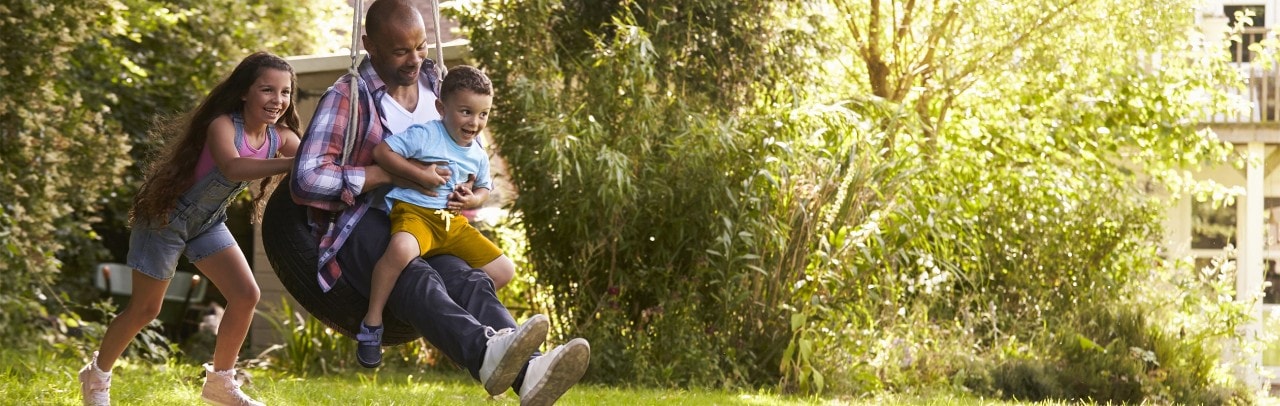 African-American girl pushing father and young brother on tire swing