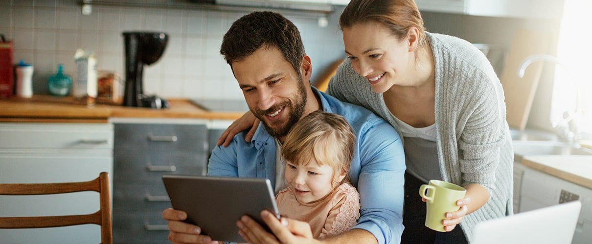 Couple with young child sitting at kitchen table looking at tablet