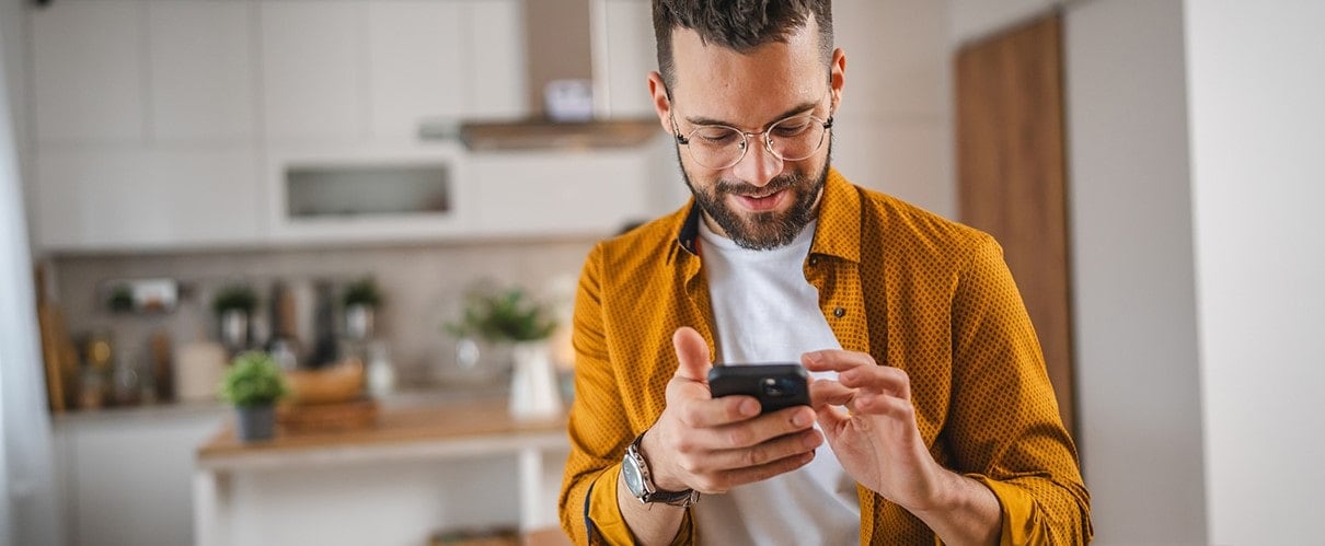 A smiling man scrolls through his smartphone