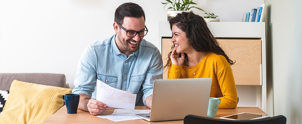 Happy couple sitting at table paying bills online
