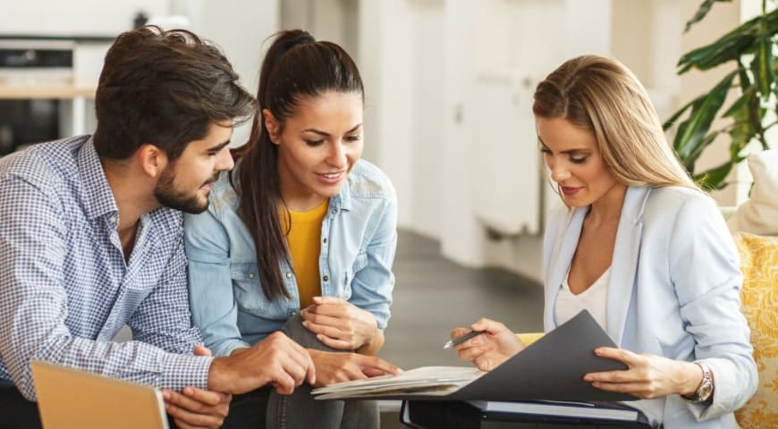 Young couple reviewing documents with female financial advisor