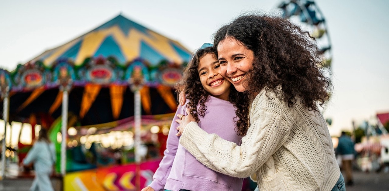 Hispanic mother and daughter smiling and hugging at an amusement park