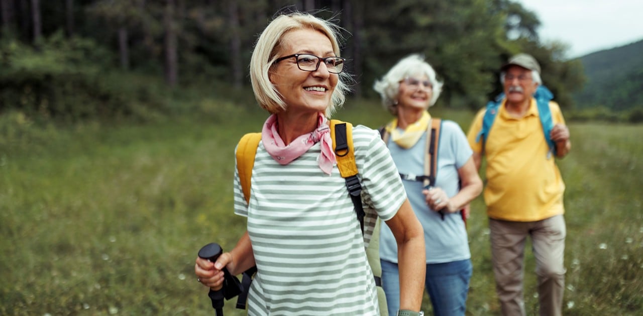 Three senior citizens hiking through a meadow