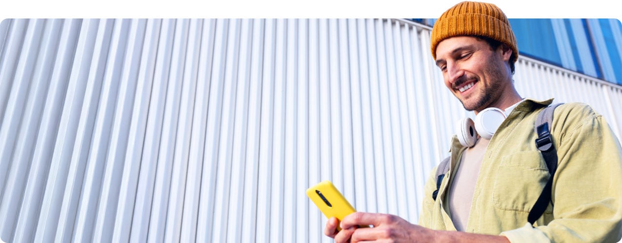 Young man wearing beanie and headphones smiling and looking at smartphone