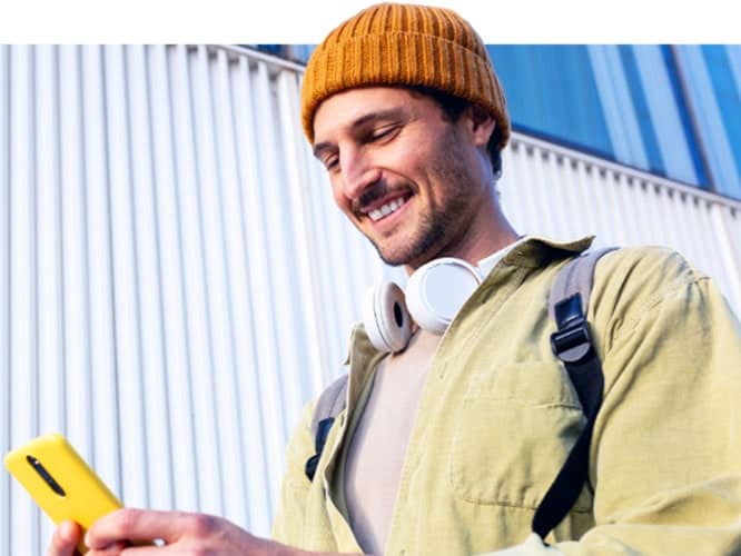 Young man wearing beanie and headphones smiling and looking at smartphone