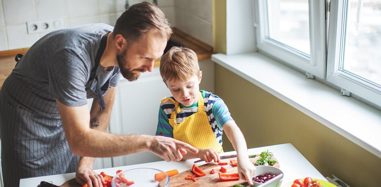 Father showing son in apron how to make a salad