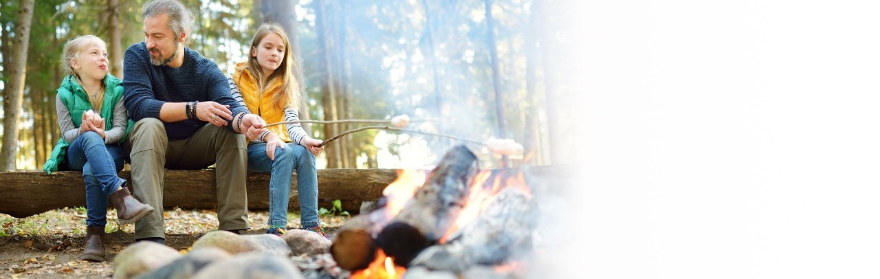 Father at campsite with two young daughters roasting marshmallows in fire pit