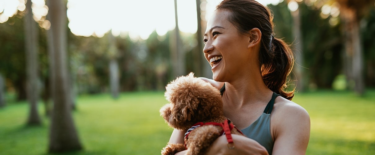 Happy Asian woman holding small, furry dog in park