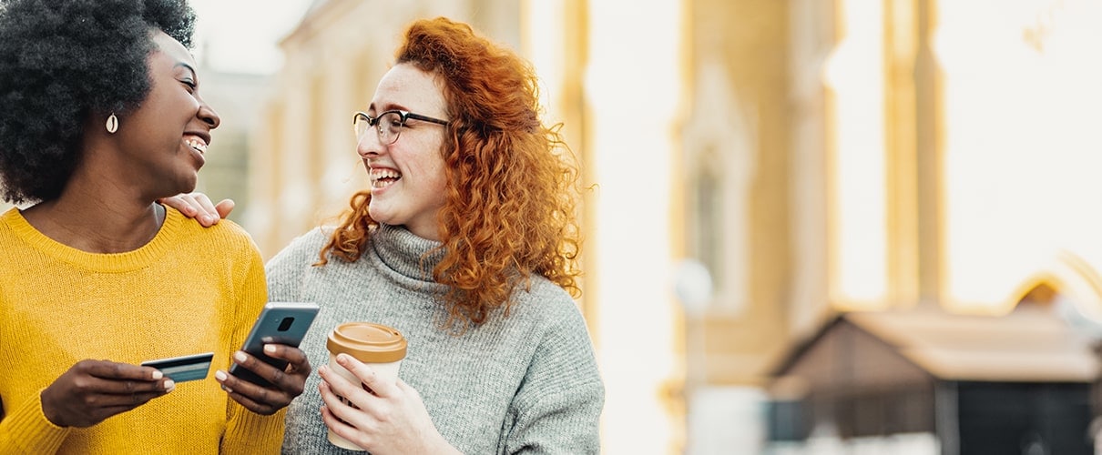 Happy diverse friends walking on downtown street holding smartphone