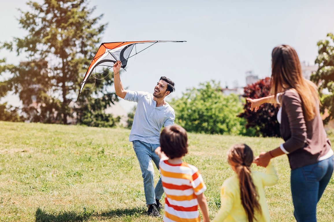 Mother and two young children watching as father flies a kite