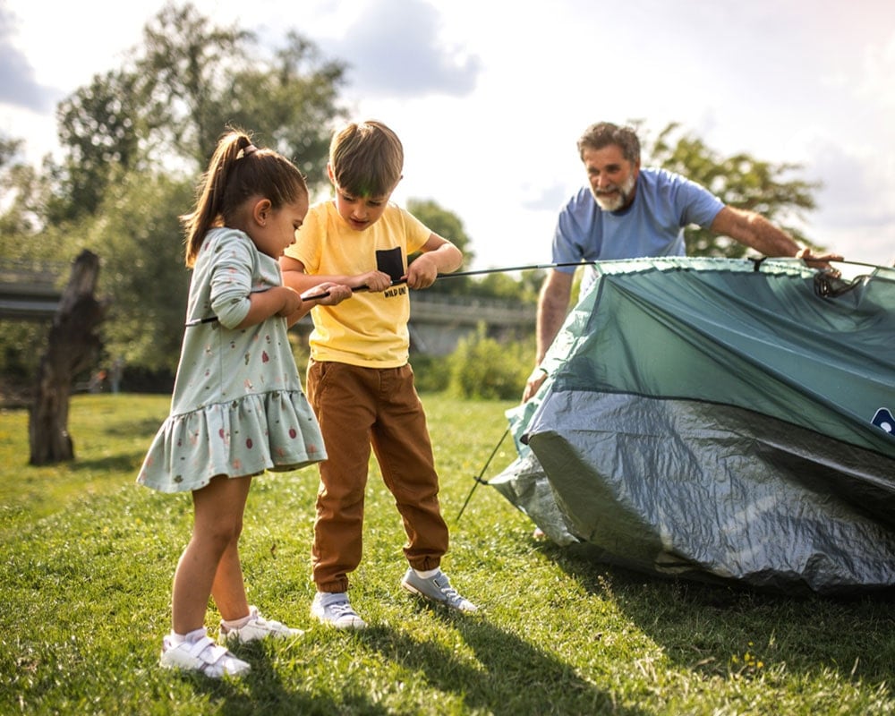 Father supervising two young children pitching a tent at a campsite