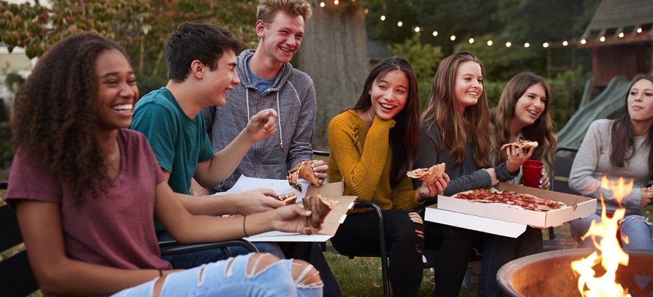 Diverse group of friends eating take-out pizza in backyard