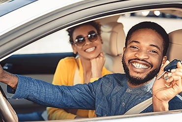 Happy African-American couple sitting in new car holding keys