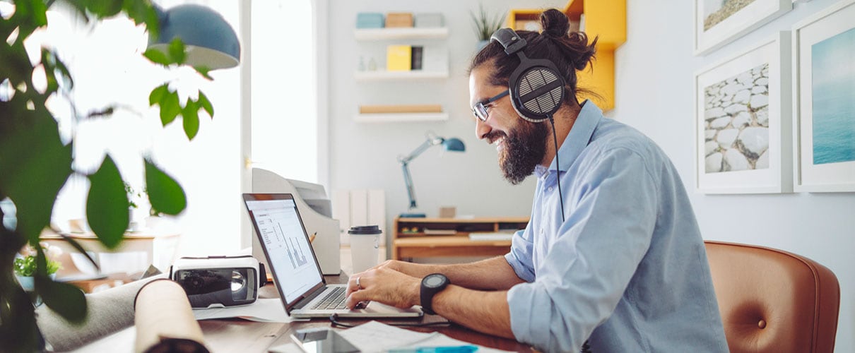Young bearded man wearing headphones and working on laptop