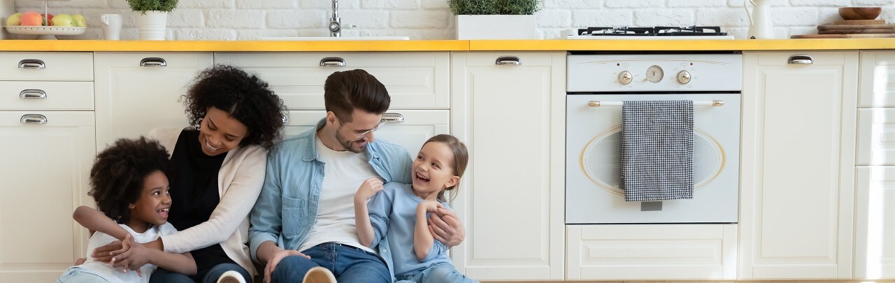 Multiethnic parents and two daughters hugging on kitchen floor