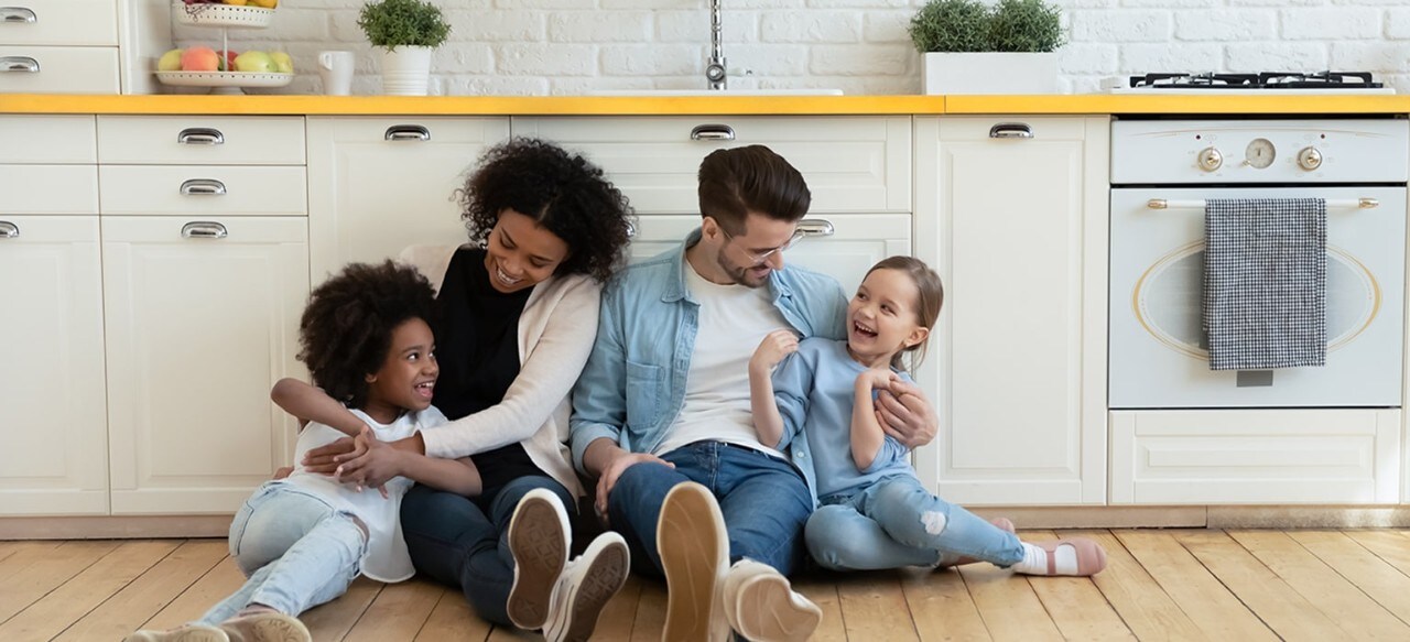 Multiethnic parents and two daughters hugging on kitchen floor