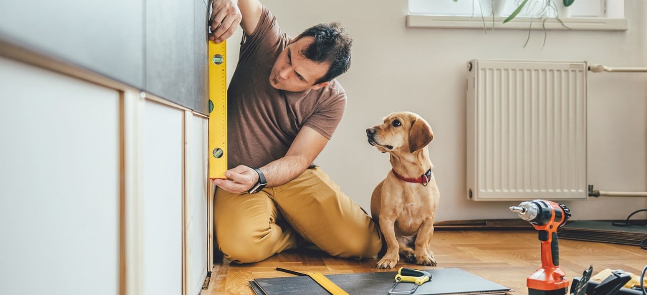 Man using level to measure wall while dog looks on