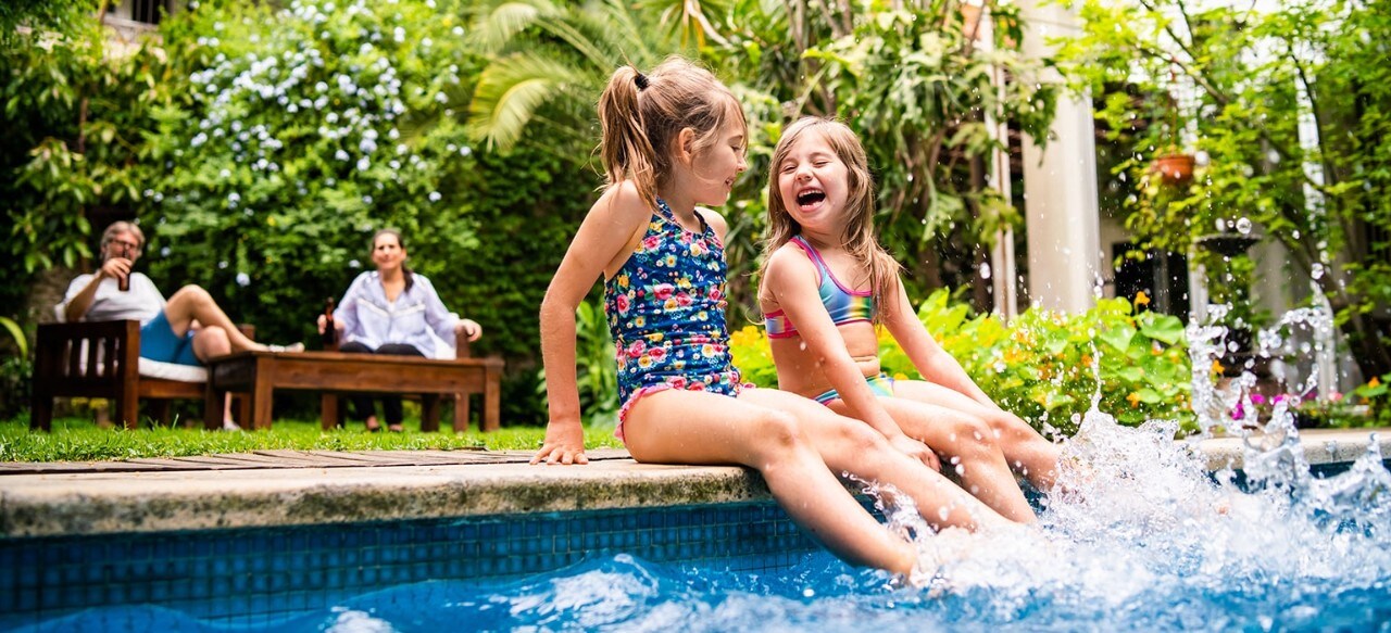 Two young sisters splashing in pool with parents looking on