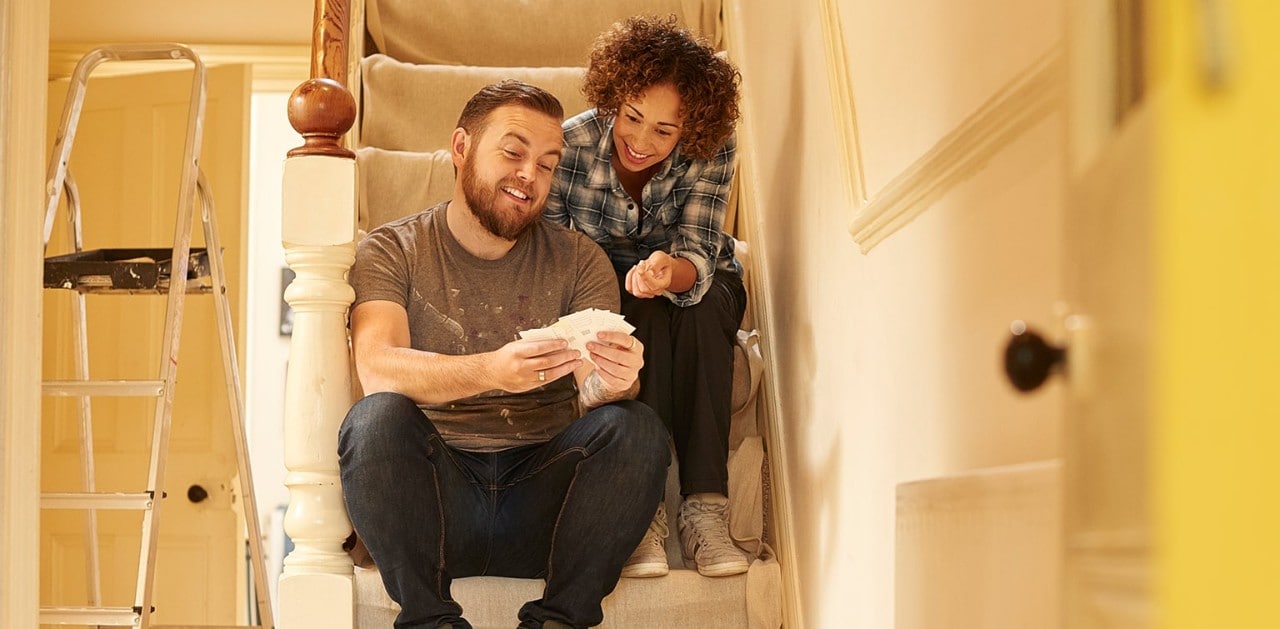Mixed race couple renovating home sitting on steps looking at paint swatches