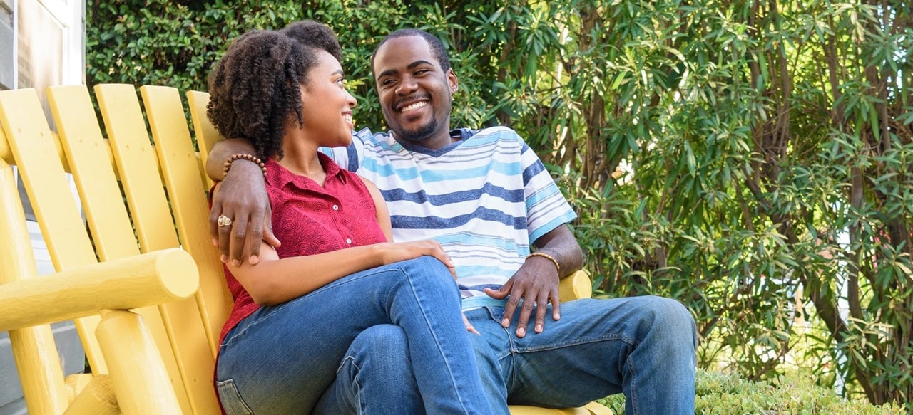 African-American couple sitting on Adirondack bench in yard