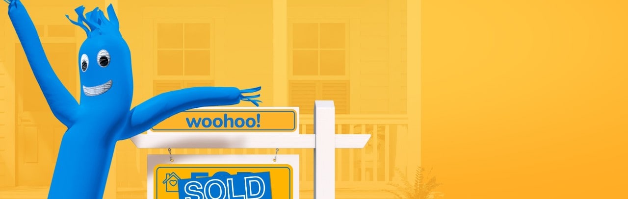Smiling blue inflatable in front of a "sold" real estate sign on yellow background