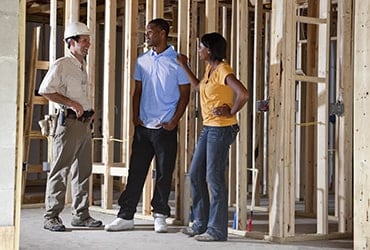 African-American couple talking to contractor in partially built home