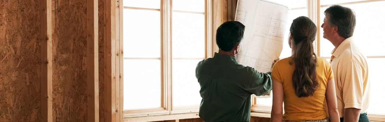 Home builder and couple reviewing blueprints inside partially built house