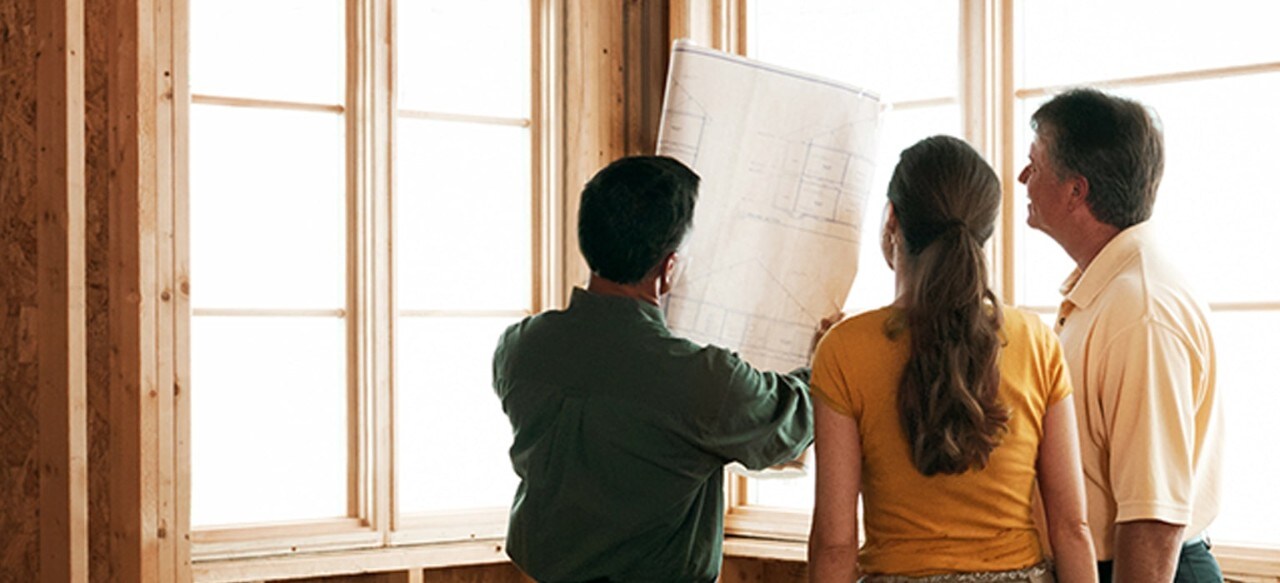 Home builder and couple reviewing blueprints inside partially built house