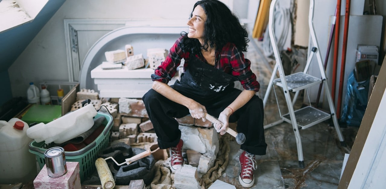 Young woman holding hammer sitting in room undergoing renovations