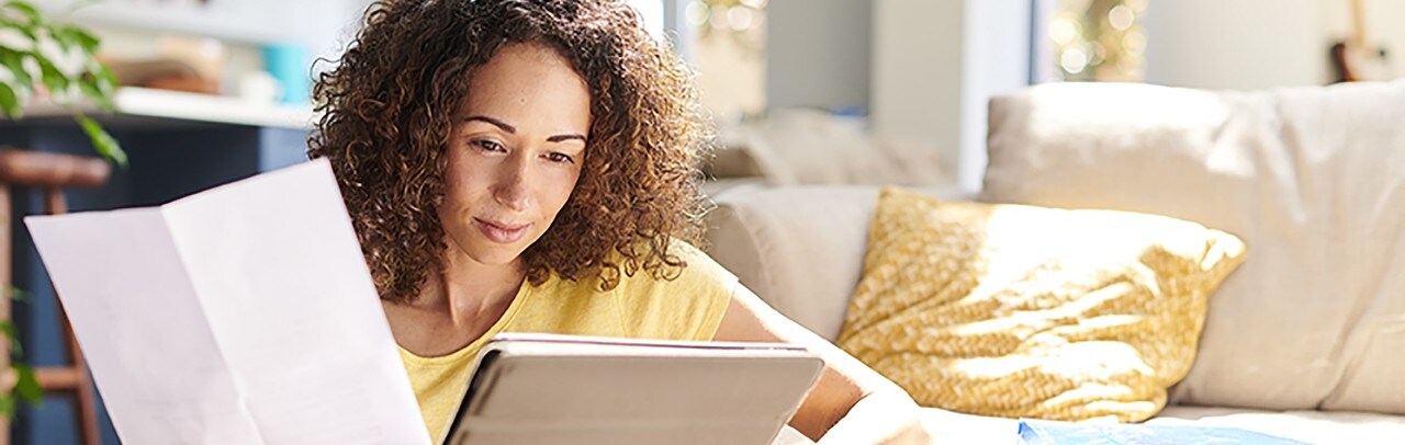 African-American woman holding financial paper and looking at tablet
